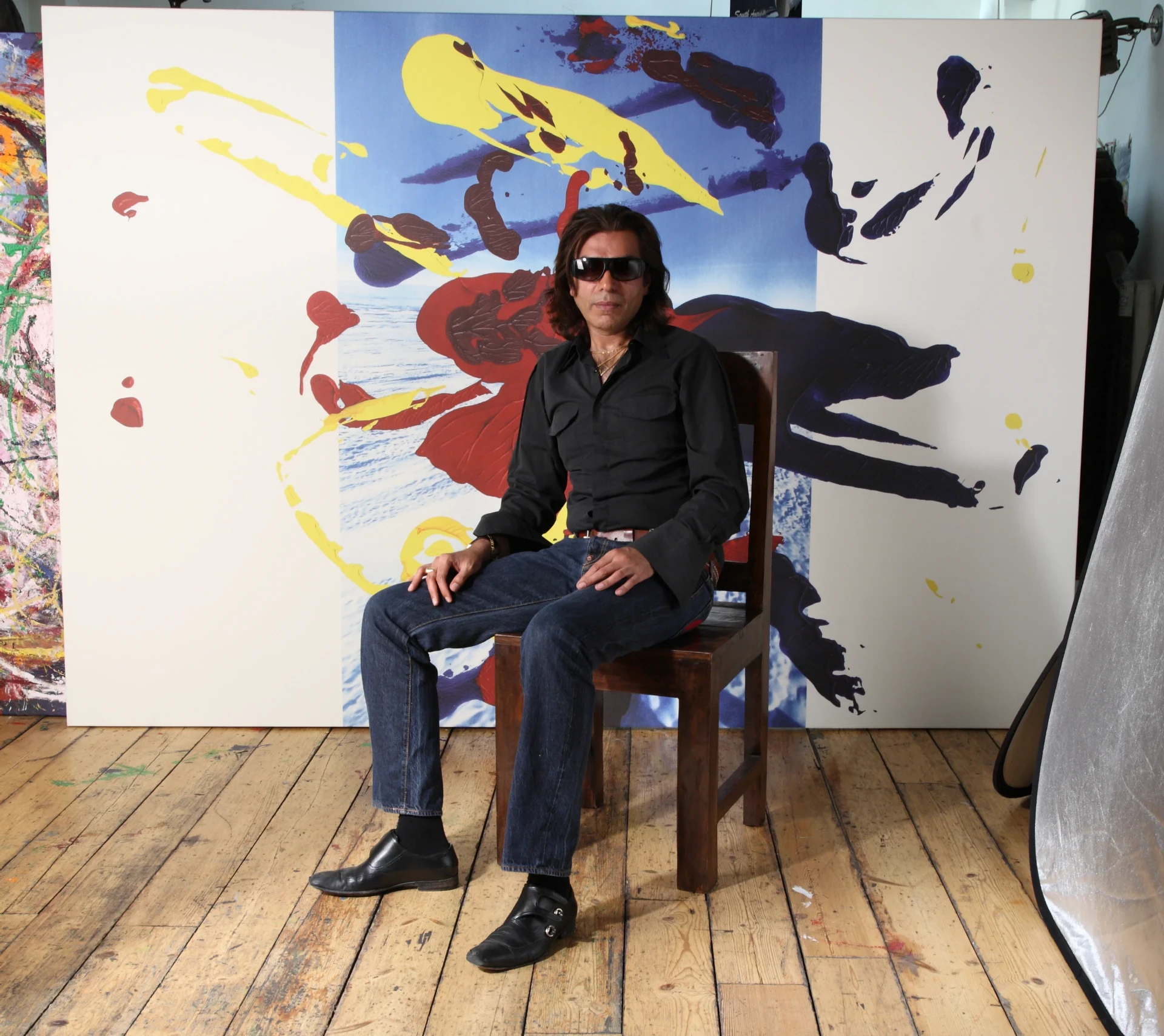 Nasser Azam, artist, seated in his London studio in front of a large abstract painting